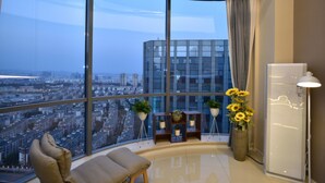 Une pièce moderne avec un plafond incurvé, de grandes fenêtres donnant sur la ville, un canapé, une petite table et des plantes en pot.