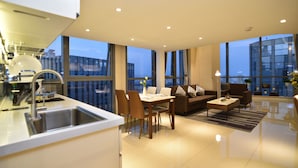 Une cuisine moderne équipée d’un évier et d’un coin repas, un salon avec un canapé et une table basse, et de grandes fenêtres offrant une vue sur la ville.