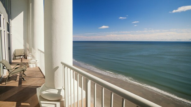 Ein Balkon mit weißen Geländern, einer Holzterrasse und Blick aufs Meer.