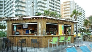 Eine Tiki-Bar mit einem Reetdach, einer Holztresore und mehreren Stühlen.