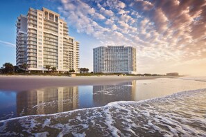A beachfront hotel with multiple floors, a sandy beach in the foreground, and a clear sky with clouds. - Spacious Oceanfront Resort with Onsite Restaurant, 5 Pools, 2 indoor Pools and Beach Access (Myrtle Beach)