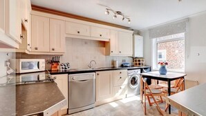 Une cuisine moderne avec des meubles de couleur claire, un lave-vaisselle, un lave-linge et un coin repas comprenant une table et des chaises.