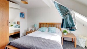 Une chambre à coucher comprenant un lit, des tables de chevet, une commode, une lampe suspendue, une fenêtre avec un rideau et une armoire.