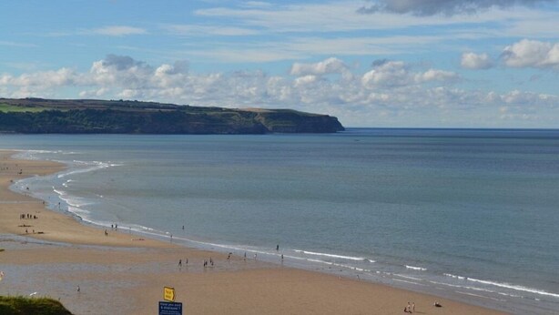 Une plage d’où l’on a une vue dégagée sur l’océan et sur une falaise éloignée.