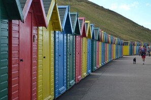 A row of colorful beach huts with sloped roofs, lined up along a walkway. - Rainbow Cottage - A home from home in the heart of Whitby (Whitby)