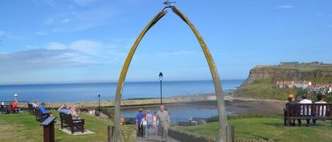 Un paseo marítimo con un arco distintivo que da acceso a la playa, bancos y una vista despejada del mar.