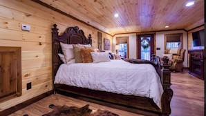 A wooden-paneled bedroom with a large bed, a wooden headboard, and a fireplace.