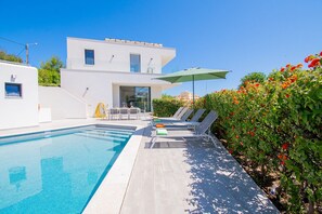 Un espace piscine moderne avec une piscine à l’eau d’un bleu limpide, des chaises longues et un bâtiment blanc en arrière-plan.