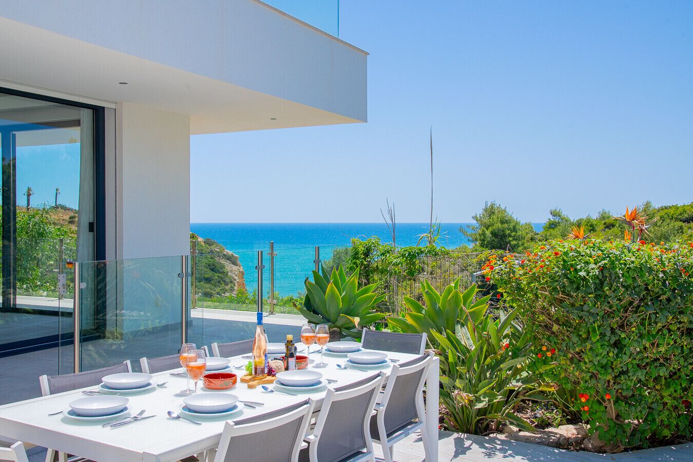 An outdoor dining area with a table set for four, overlooking a coastal view.