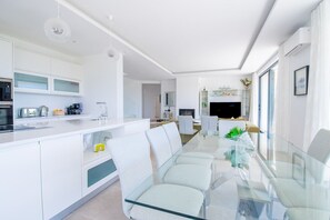 Une cuisine moderne avec des meubles blancs, une table à manger en verre et un îlot central.