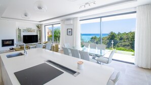 A modern kitchen with a large island, a dining area with a glass table, and a view of the sea. - Villa Centeanes Luxury villa,enviable position stunning sea views! (Carvoeiro)