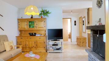 Een woonkamer met een televisie, houten kasten, een bank, een salontafel en een open haard.