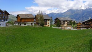 Une rangée de maisons en bois dotées de balcons, se dressant sur un fond de montagnes et d’un ciel dégagé.
