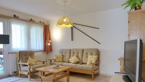 Un salon avec un canapé, des fauteuils, une table basse et un téléviseur posé sur un meuble.