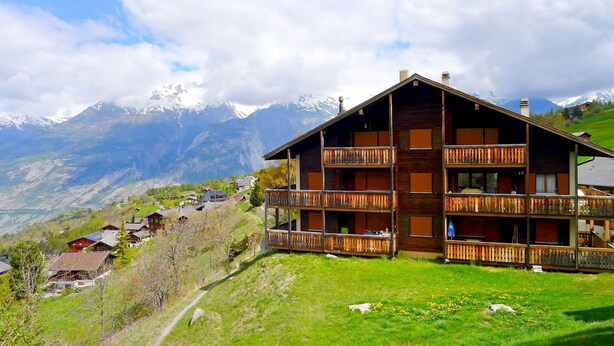 Un chalet doté de plusieurs balcons, avec une vue sur les montagnes et un ciel dégagé.