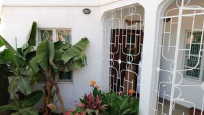 A white building with a gated entrance, large green plants, and a potted flower arrangement.