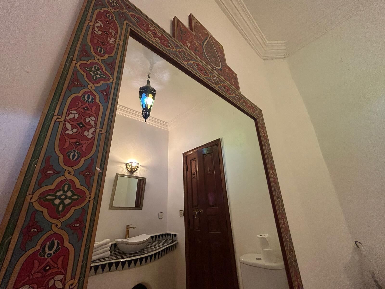 A bathroom with a large mirror, a sink, a toilet, and a decorative wall panel.