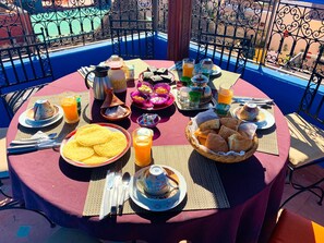 A round table set with breakfast items, including bread, eggs, and beverages, on a balcony with a blue railing. - 19th century traditional Riad located in the heart of the medina (Marrakech)
