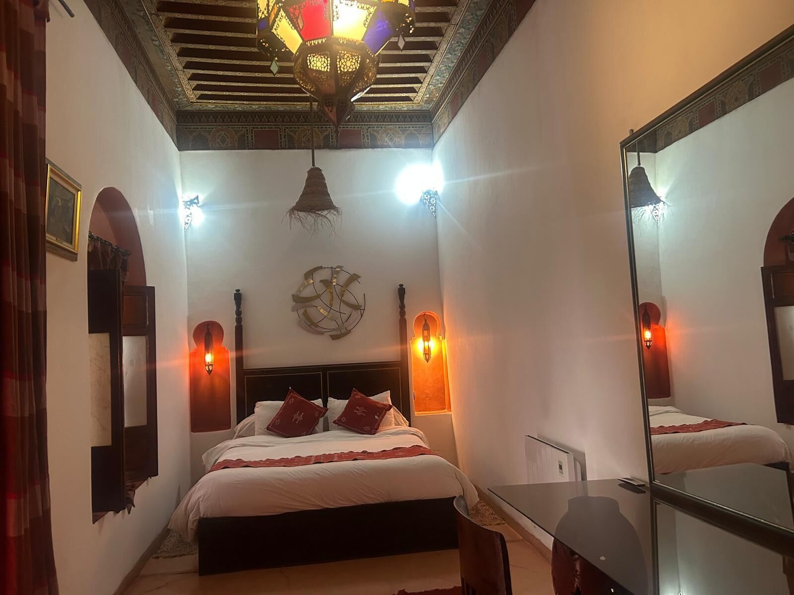 A bedroom with a bed, bedside lamps, a mirror, and a chandelier.
