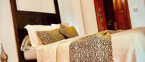 Quarto com uma cama, tapete vermelho estampado, almofadas decorativas e uma porta de madeira.