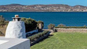 A coastal view with a stone pathway leading to a grassy area, a stone wall, and a clear view of the sea and distant hills. - Beachfront villa with stunning sea view . (Paros)