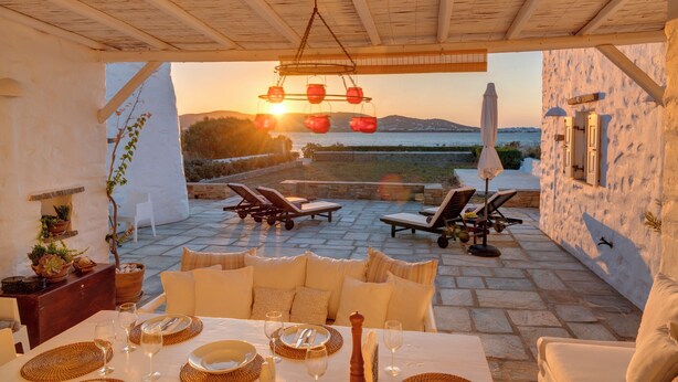 A sunlit outdoor dining area with a table set for two, overlooking a scenic coastal view. - Beachfront villa with stunning sea view . (Paros)