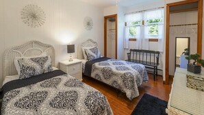 A bedroom with two beds, a ceiling fan, a nightstand, a chair, and a window with curtains. - Pet Friendly 3 Bedroom 5 Minutes to Town. (Cape May)