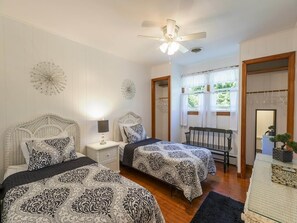 Ein Schlafzimmer mit zwei Betten, einem Deckenventilator, einem Nachttisch, einem Stuhl und einem Fenster mit Vorhängen.