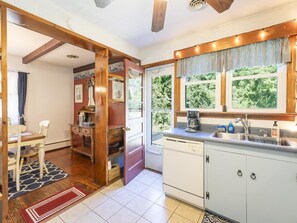 A kitchen with a dishwasher, a coffee maker, and a window with curtains.