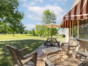 Eine Terrasse mit Korbmöbeln, einem Picknicktisch und einem Sonnenschirm.