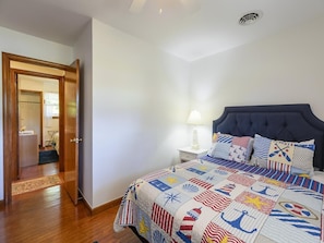 Une chambre à coucher comprenant un lit, une table de chevet, une lampe et une porte donnant sur une autre pièce.