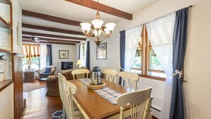 A dining area with a wooden table, white chairs, a chandelier, and a view through large windows. - Pet Friendly 3 Bedroom 5 Minutes to Town. (Cape May)