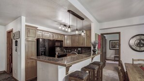 A kitchen with wooden cabinets, a granite countertop, and a bar stool seating area.