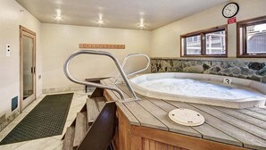 A hot tub with a wooden deck, a clock, and a stone wall.