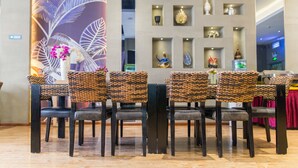 Un comedor con sillas de mimbre y una mesa, una pared con adornos, y un gran mural floral.