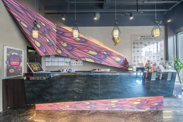 A reception desk with a black marble top, colorful abstract wall art, and hanging pendant lights.