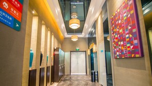 Un pasillo de hotel con señalización, una alfombra estampada y una obra de arte colorida en la pared.