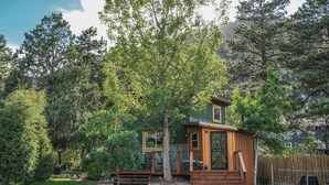 A small wooden cabin with a porch, surrounded by trees and a wooden fence.