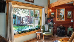 A cozy room with a large window, a wooden chair, a small table, and a vintage stove.