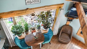 A cozy room with a wooden ceiling, a dining table with chairs, potted plants, and a sign reading 'The House'.