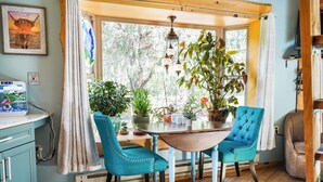 A dining area with a wooden table, two teal chairs, and a variety of potted plants.