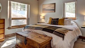 A bedroom with a wooden ceiling, a bed with a patterned blanket, two bedside lamps, and a painting on the wall. - Breck Cabin, Ten Mile Range Views, Wrap Deck, Fireplaces, Sleeps 6 (Breckenridge)
