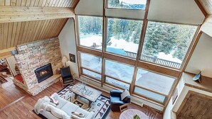 A cozy living room with a stone fireplace, large windows, and a view of a snowy landscape. - Breck Cabin, Ten Mile Range Views, Wrap Deck, Fireplaces, Sleeps 6 (Breckenridge)