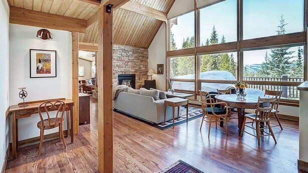 A spacious living area with a fireplace, large windows, and a view of the outdoors. - Breck Cabin, Ten Mile Range Views, Wrap Deck, Fireplaces, Sleeps 6 (Breckenridge)