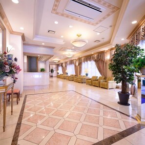 A hotel lobby with a reception desk, seating area, and a large potted plant. - Hotel Capital in Yamagata (Yamagata)