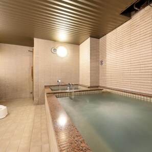 A spa area with a rectangular hot tub, tiled walls, and a ceiling with linear light fixtures. - Hotel Capital in Yamagata (Yamagata)