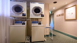 A hotel laundry room with two Sanyo CO/N DRYER 45 machines, a coin-operated washing machine, and a small table with a checkered tablecloth. - Hotel Capital In Yamagata (Yamagata)