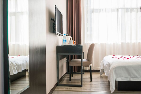 Una habitación de hotel con una cama, un escritorio con silla, televisión y ventana con cortinas.
