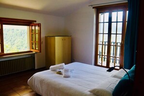 A hotel room with a large bed, a window with a view of a forest, a wardrobe, and a radiator.
