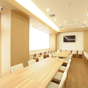 A conference room with a long table, chairs, a projector screen, and a mounted TV. - Ab Hotel Omihachiman (Omihachiman)